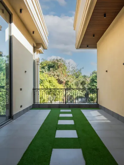 A simple yet elegant balcony space in the Sultanpur farmhouse. The design uses artificial turf with stone pavers to create a green, low-maintenance outdoor area that feels connected to the surrounding nature.