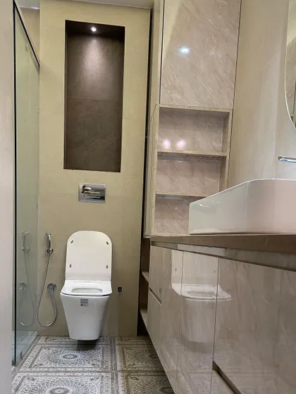 This bathroom combines a floating vanity with a marble-like finish and beautiful patterned floor tiles. A tall, lit niche next to the toilet provides space for decor or toiletries.