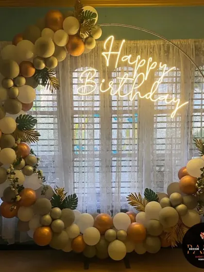 An elegant ring decoration with muted green, gold, and white balloons, accented with artificial leaves for a touch of nature.