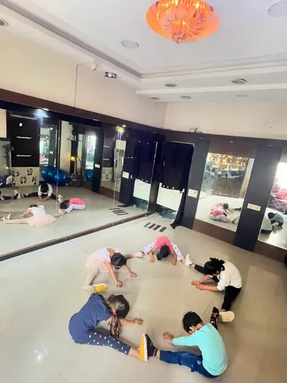 A wider view of the kids' dance class doing their warm-up stretches in a circle, with their reflections in the studio mirror.