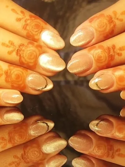 An elegant design perfect for a wedding guest or festive occasion, featuring shimmery nude nails with a delicate gold accent, paired with henna-adorned fingers.