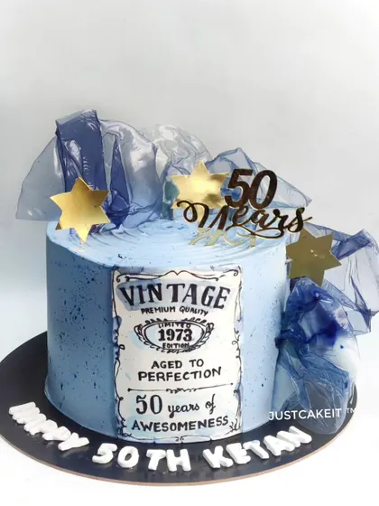 An abstract-style 50th birthday cake with a hand-painted vintage label. The design uses a cool blue palette and edible rice paper sails.