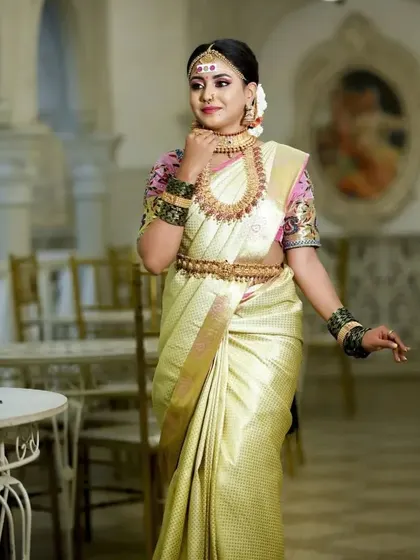 A bride in a beautiful off-white silk saree, adorned with our classic temple jewellery. The contrast of the pink blouse and gold jewellery is stunning.