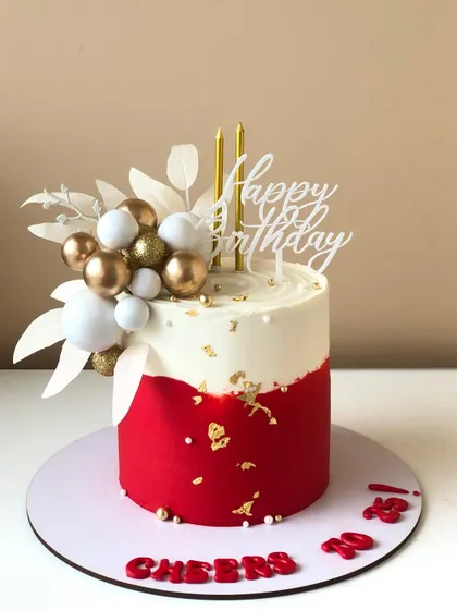 A bold and modern cake in red and white, with gold leaf accents and a stylish balloon cluster.