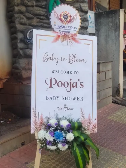 A "Baby in Bloom" welcome sign for Pooja's baby shower, decorated with our company logo and a fresh flower base.