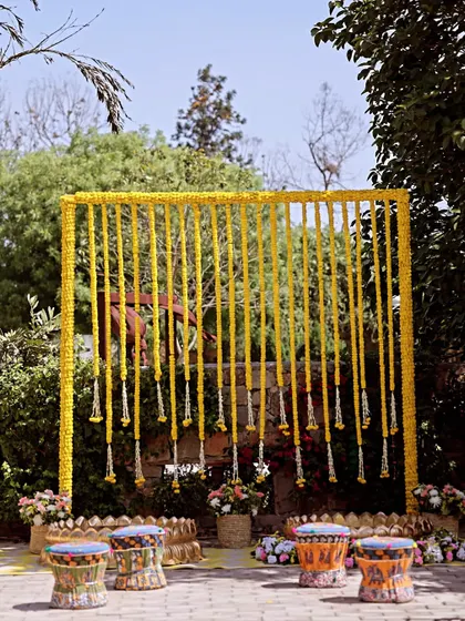 A minimalist yet beautiful Haldi backdrop with a frame of hanging marigold garlands, perfect for an outdoor setting.