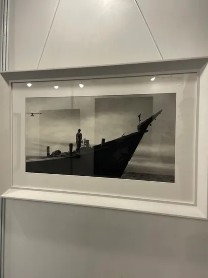 'Serene', an 18 by 36 inch charcoal drawing on white paper, shown here framed at an exhibition. The artwork captures a tranquil moment on the water.