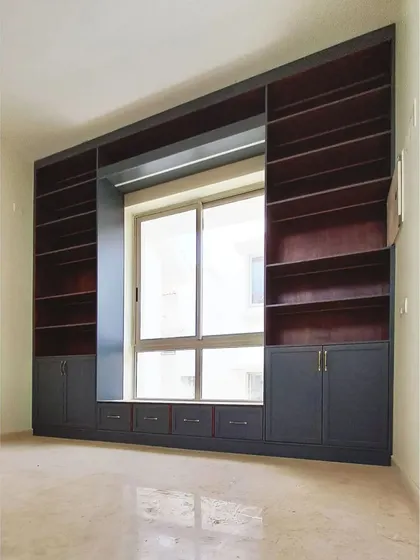 The library unit before it's filled with books, showcasing the ample shelving, the window seat, and the lower cabinets. The dark grey and wood two-tone finish adds a touch of modern sophistication.