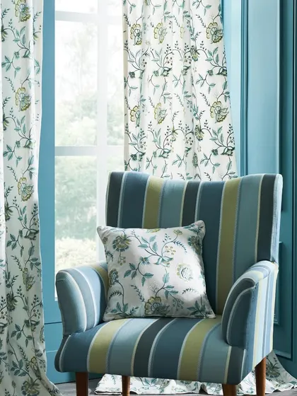 A close-up of a striped armchair paired with floral curtains against a vibrant teal wall. This image highlights the art of mixing patterns within a complementary color palette for a confident design statement.