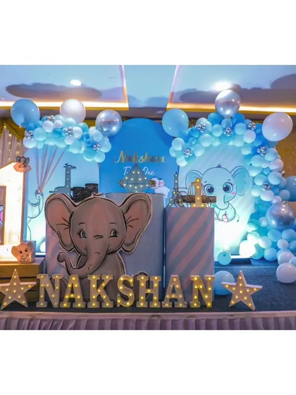 A sweet baby elephant theme for Nakshan's first birthday. The stage is decorated in shades of blue with elephant cutouts, marquee letters, and star-shaped lights.