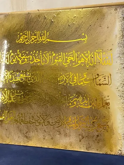 A side view of the brown and gold Ayat al-Kursi artwork, showing its scale and the texture of the embellished borders.