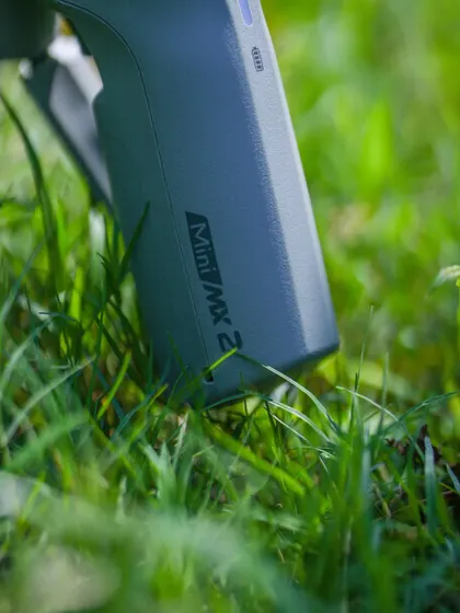 A product shot of the MOZA Mini MX2 gimbal in a natural, outdoor setting. This highlights the gear's portability and readiness for any adventure.