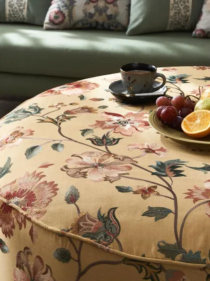 A close-up of a large ottoman upholstered in a beautiful floral fabric. The shot is styled with a cup of coffee and fruit to create a warm and inviting 'at-home' feel.