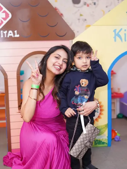 A mother and son flash peace signs for the camera while playing in the pretend-play area.