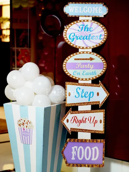 A classic carnival-style signpost directing guests to 'The Greatest Party on Earth', food, and games, next to a giant popcorn box prop.