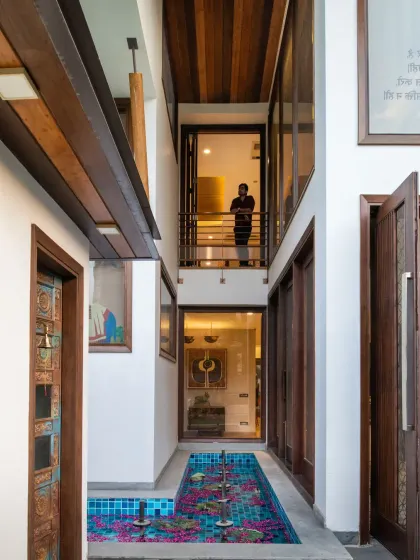 The front of the Ashraya Residence is characterized by expansive open spaces. Voids and cut-outs in the design facilitate ample natural light and foster visual connectivity between different levels, as seen in this view of the entrance corridor.