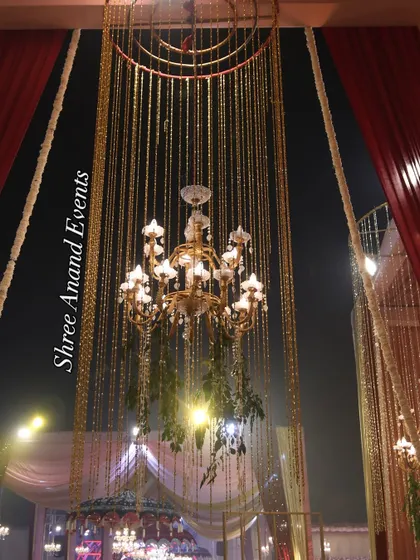 A magnificent hanging chandelier, adorned with greenery and surrounded by a cascade of golden strings, creating a stunning light fixture.