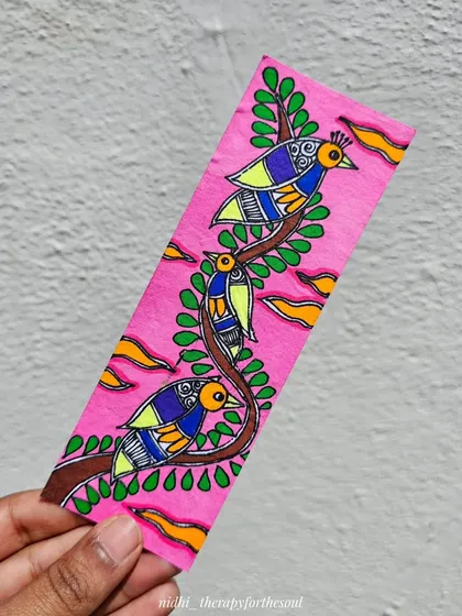 This pink bookmark features a trio of birds on a branch, painted in a colorful Madhubani style.