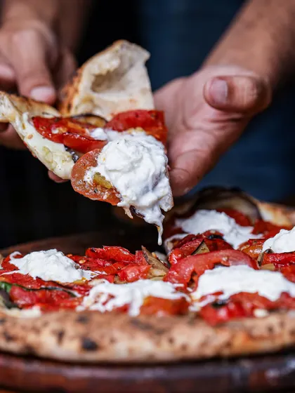 A perfect slice being lifted, showcasing the melted cheese and soft, airy crust. This pizza is topped with roasted peppers and dollops of fresh ricotta.