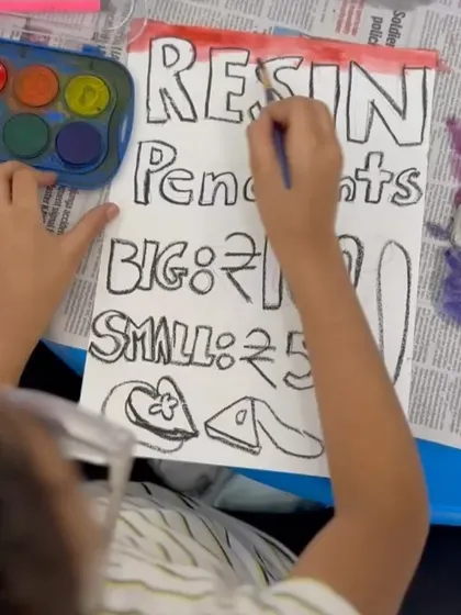 A student carefully paints a sign for the resin pendants he created, learning about pricing and marketing in a hands-on way.