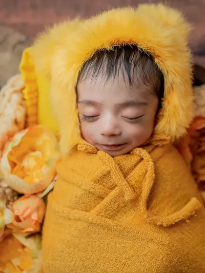 A smiling sleepy face. This close-up captures a moment of pure bliss from the baby in the fuzzy yellow hood.