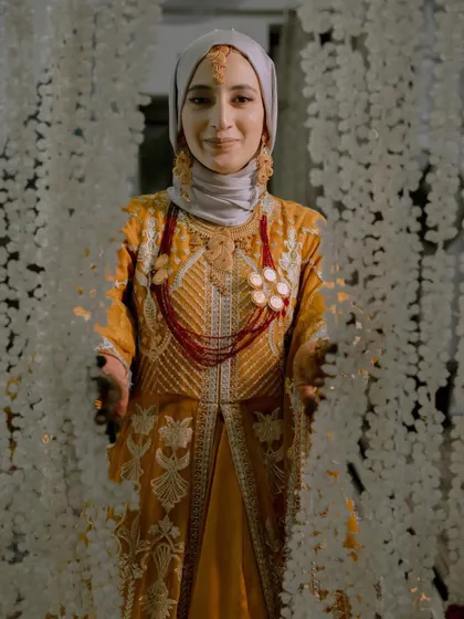 A welcoming portrait of the bride, Insha, smiling from behind a curtain of flowers, a beautiful moment from her Nikah ceremony.