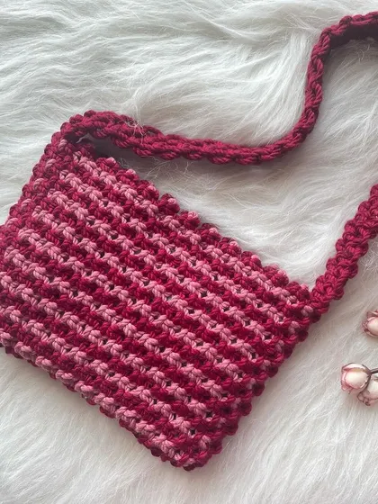 This shoulder bag showcases a beautiful two-tone pattern using shades of red and pink. The simple, rectangular shape makes it a versatile choice for daily wear.