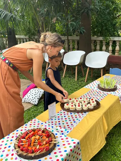A mother and daughter picking out treats from the colorful food table. I design my kids' party spreads to be visually exciting, with items like fruit skewers and mini sandwiches.