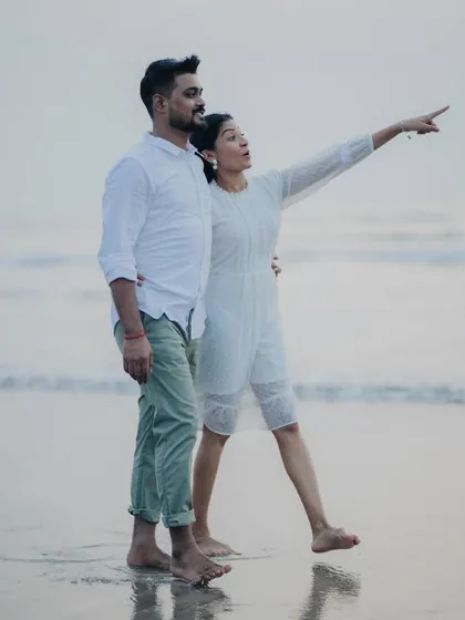 A candid pre-wedding moment on the beach, where the bride-to-be points excitedly towards the horizon, sharing a discovery with her partner.