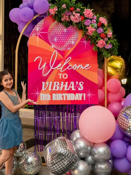 The birthday girl proudly welcoming guests to her disco party next to the colorful entrance sign.