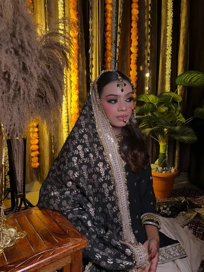 A full portrait of a bride in a traditional black and gold outfit. The setting with marigold flowers adds a festive touch to this unique look.