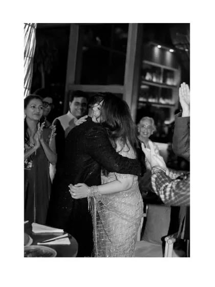 A beautiful black and white photo of a celebratory hug at Juhi and Jay's engagement party, surrounded by the happy faces of their loved ones.