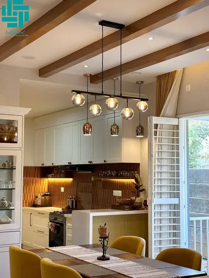 A view from the dining table towards the kitchen and balcony. The wooden ceiling beams and large windows with sheer curtains create a bright and airy atmosphere.