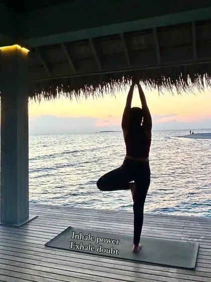 Finding stillness in Vrikshasana, the Tree Pose, as the sun sets. This pose is all about balance, focus, and rooting down to feel stable. The message on my mat, "Inhale power, Exhale doubt," is a core part of my teaching, focusing on breathwork to build mental and physical strength.