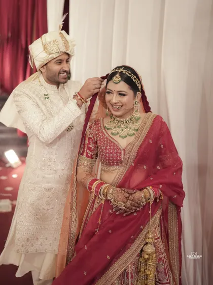 A sweet, candid moment where the groom helps adjust his bride's dupatta. These small acts of care make for beautiful, heartfelt photographs.