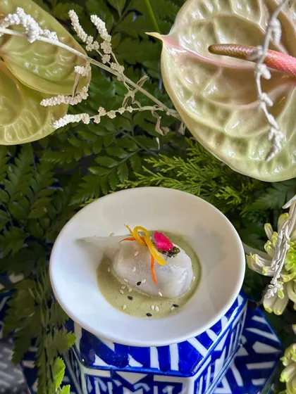 A Thai Basil Dumpling resting in a flavourful green curry dressing, garnished with delicate vegetable slivers. A taste of Southeast Asia in one perfect bite.
