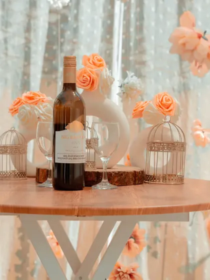 A close-up view of the details within my hanging floral canopy setup. A bottle of wine, elegant glassware, and delicate birdcage props add layers of sophistication to the romantic scene.