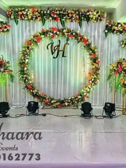This reception stage features a large floral ring as the centerpiece, personalized with the couple's initials. The setup is complemented by floral arrangements on vintage-style bicycle props for a unique, rustic touch.
