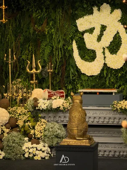 The main altar for the Ganesh ceremony, with a floral 'Om' symbol, trishuls, and a golden mouse statue, all beautifully arranged.