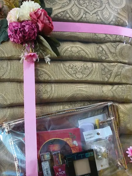 A stack of golden sarees packed with a small pouch of cosmetics and jewelry.