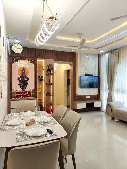 A wide shot of a living and dining area, where the custom pooja unit is a prominent and beautiful feature, seamlessly integrated with the TV unit and overall decor.