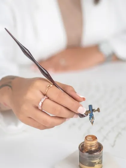 A close-up shot of me at my desk, dipping my calligraphy pen into a pot of golden ink. This image captures the focus and intention behind the art form, a moment of quiet before the writing begins. It's a practice of believing in your own potential.