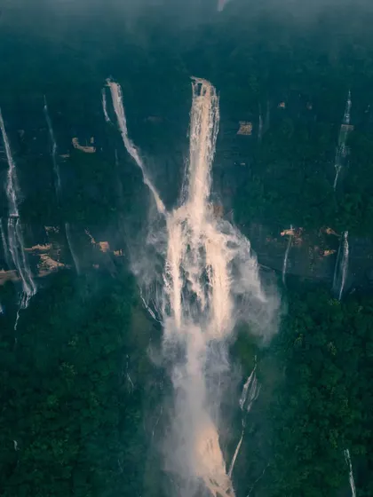 An aerial shot of Nohkalikai Falls, appearing like a brushstroke of white against the deep green canvas of Meghalaya's forests.