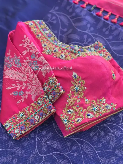 A pink blouse with multi-color floral embroidery on the sleeves and neckline.
