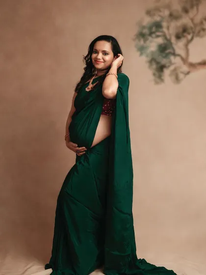 A full-length portrait of a mom-to-be in a green saree, showing off her beautiful baby bump. The simple backdrop keeps the focus on her.