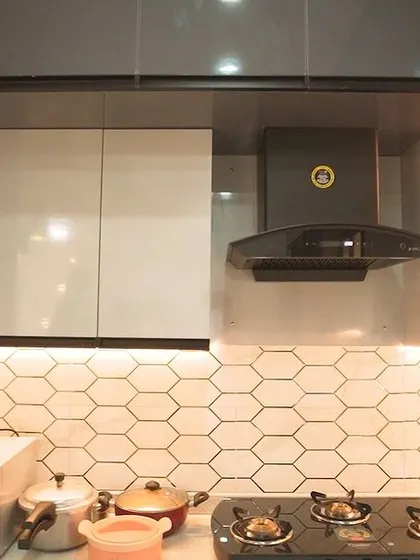 A modern kitchen featuring a white hexagonal tile backsplash. The under-cabinet lighting creates a warm glow, highlighting the geometric pattern and making the space feel cozy and inviting.