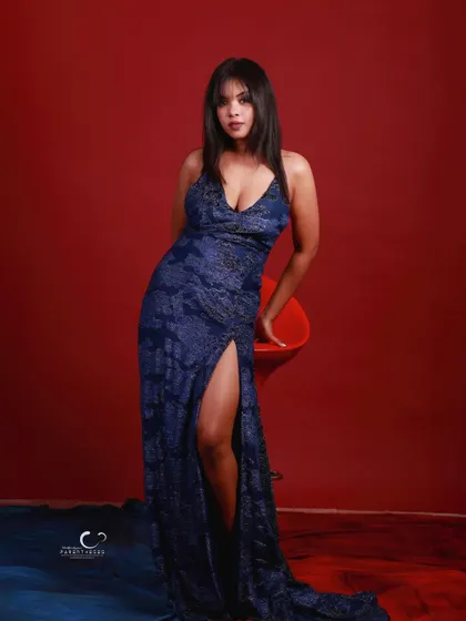 A confident and alluring pose leaning against a red stool. The composition highlights the elegant lines of the gown.