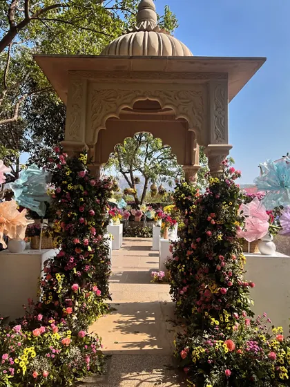 An elegant entrance to a floral-themed event, with a traditional Jarokha-style archway flanked by pillars of vibrant pink and yellow flowers.
