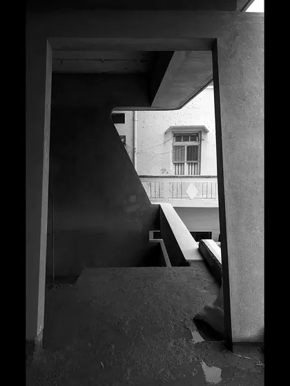 A composition of geometric shapes and shadows seen through a doorway on a construction site, highlighting the abstract beauty of the raw structure.
