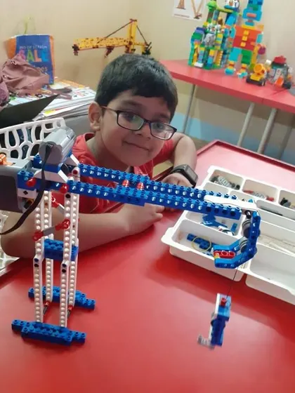 A student smiles after successfully building a robotic arm, a project that teaches principles of levers, gears, and automated movement.
